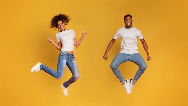 Carefree black millennial man and woman jumping in air, having fun on orange studio background - Photo, Image