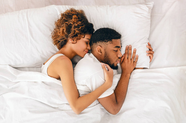 schwarze Frau umarmt ihren Mann und lächelt, genießt den gemeinsamen Schlaf im Bett, Draufsicht mit Leerraum - Foto, Bild