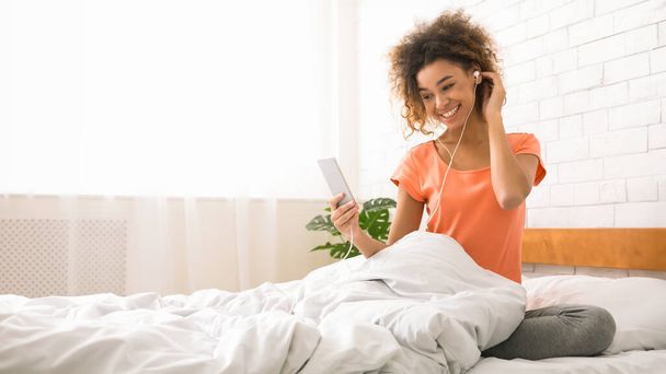 Happy lady écouter de la musique avec smartphone, assis dans le lit le matin - Photo, image