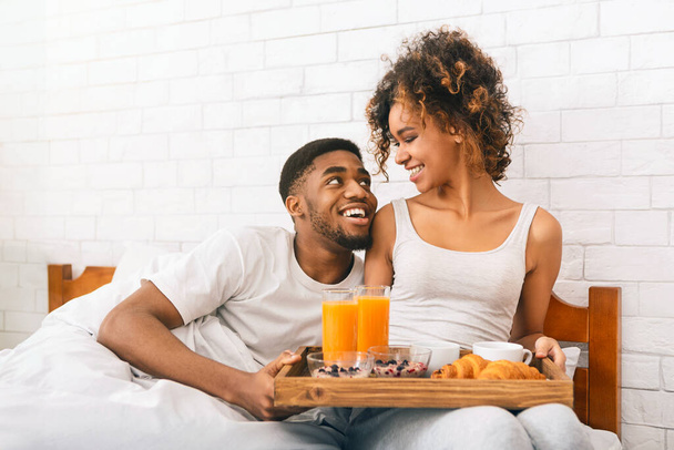 Wake up with breakfast in bed for true love. Loving african-american couple cuddling with food, free space - Photo, Image