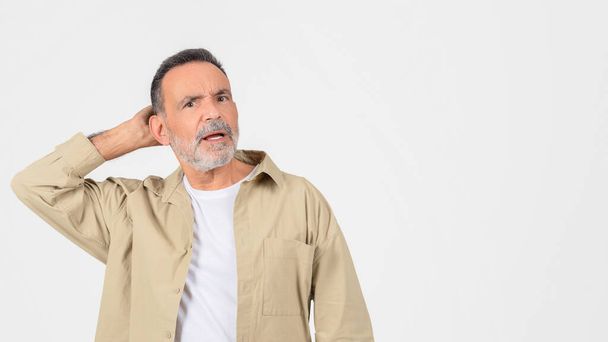 Puzzled older man scratching his head in a gesture of confusion or forgetfulness on a plain white background - Photo, Image