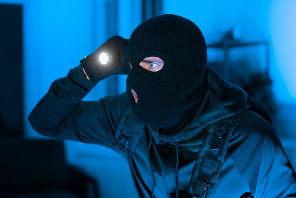Un escenario intenso con una persona usando un pasamontañas usando una linterna, posiblemente para una escena del crimen - Foto, Imagen