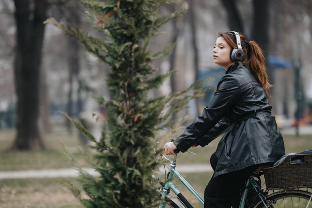 Een jonge, aantrekkelijke zakenvrouw in stijlvolle kleding fietst in een parkomgeving, straalt zelfvertrouwen en elegantie uit. - Foto, afbeelding