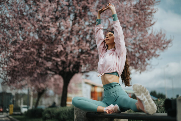Młoda kobieta bierze udział w sesji jogi na świeżym powietrzu, otoczona kwitnącymi wiśniami w świeżości wiosny. - Zdjęcie, obraz