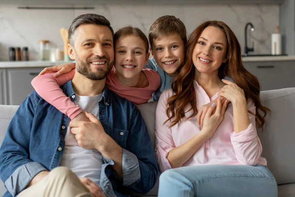 Довольная семья из четырех родителей, дочери и сына позирует с улыбками для случайного портрета на диване в гостиной - Фото, изображение