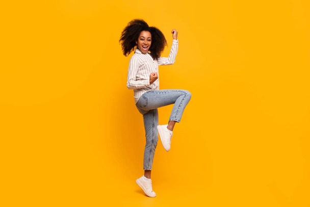 Ecstatic African American woman with curly hair dancing and enjoying herself against a yellow backdrop - Photo, Image