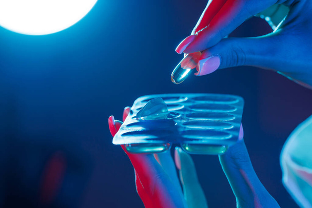 рука достает таблетку из упаковки крупным планом в ультрафиолетовом цвете - Фото, изображение