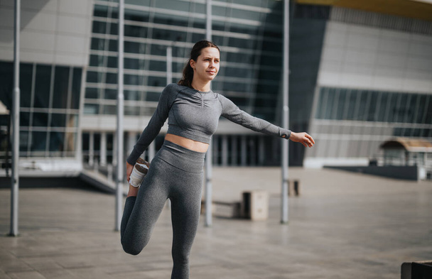 Una joven atlética hace una pausa para un estiramiento pre-ejercicio en un entorno urbano, abrazando un estilo de vida saludable. - Foto, imagen