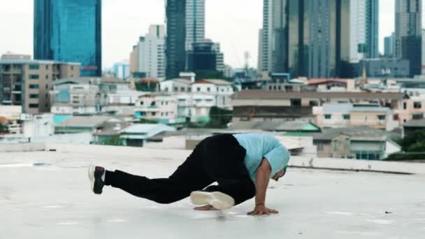 Профессиональная кавказская танцовщица B-boy практикует уличные танцы на крыше с городом или городом. Съемка движения молодого человека, исполняющего уличные танцы, в позе "стоп". Открытый спорт 2024. Хипоп. - Кадры, видео