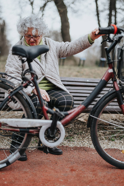 Alegre jubilada madura disfrutando de actividades al aire libre, descansando con su bicicleta en un entorno de parque. - Foto, Imagen