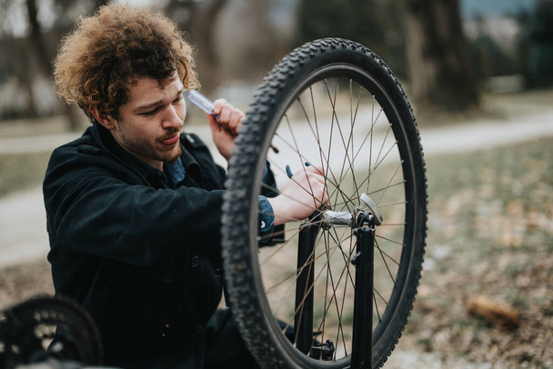 Młody przedsiębiorca naprawia rower w parku, łącząc biznes ze zdrowym stylem życia. - Zdjęcie, obraz