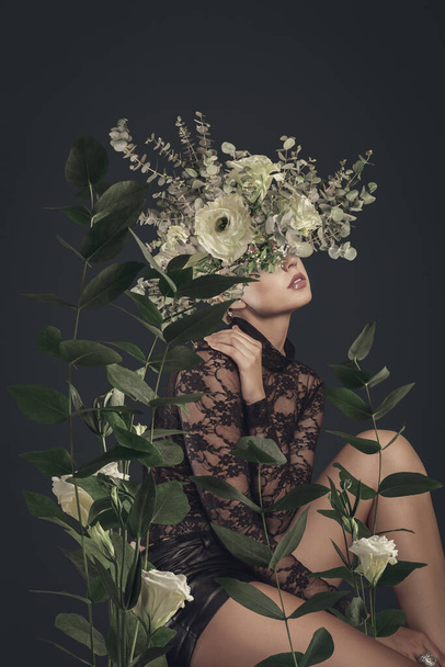 A sensual woman with floral headdress poses amidst lush leaves and blooms in an artistic botanical portrait. - 写真・画像