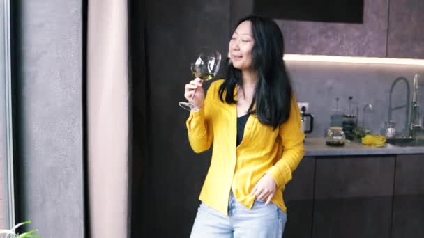 Asijské žena držení sklenice s vínem při pohledu z okna v kuchyni doma. - Záběry, video