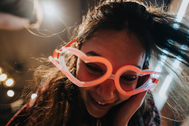 Close-up of a cheerful young lady wearing novelty glasses, enjoying fun times with friends indoors. - Photo, Image