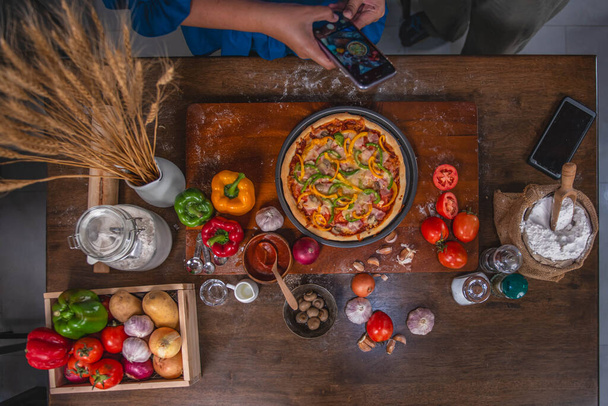 Widok z góry, kucharka za pomocą smartfona Zrób zdjęcie pizzy na talerzu. które robi w swojej domowej kuchni z pomysłem na domowe jedzenie i pizzę. - Zdjęcie, obraz