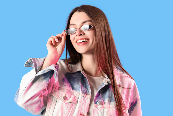 Jeune femme dans des lunettes de soleil élégantes sur fond bleu - Photo, image