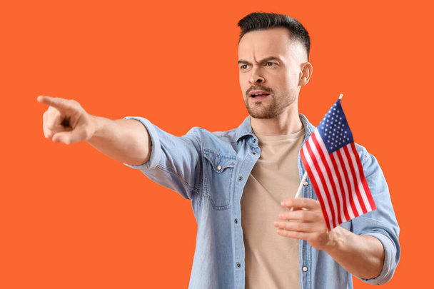 Junger Mann mit USA-Fahne zeigt auf etwas auf orangefarbenem Hintergrund. Anschuldigungskonzept - Foto, Bild