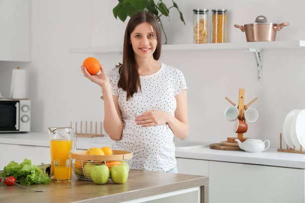 Mulher grávida bonita com laranja na cozinha - Foto, Imagem