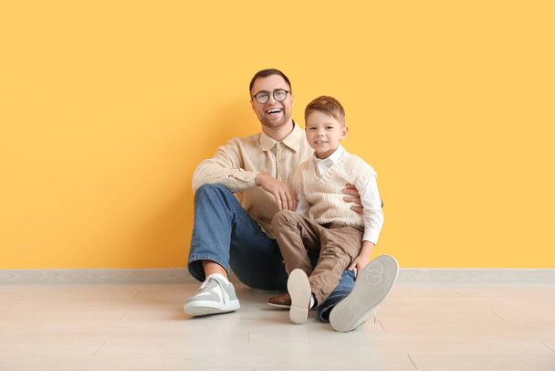 Щасливий батько і його маленький син сидить біля жовтої стіни - Фото, зображення
