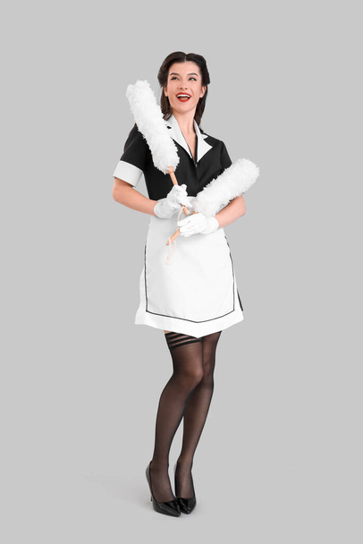 Beautiful pin-up chambermaid with dust brushes on grey background - Photo, Image
