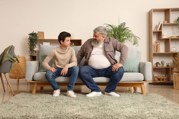 Onnellinen isoisä ja hänen söpö pojanpoikansa istuu sohvalla kotona - Valokuva, kuva