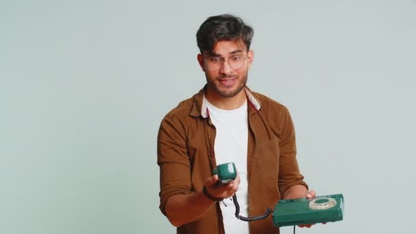 Hey you, call me back. Indian young man talking on wired landline vintage telephone of 80s, advertising proposition of conversation, online shopping, hotline. Arabian guy isolated on gray background - Footage, Video