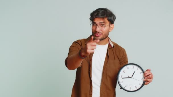 それはあなたの時間です,急いで. ウォールオフィスの時計に時間を表示するインドの若者は,いいえ,親指を上げ,承認し,カメラ,広告,締め切りで指を指します. スタジオグレーの背景に孤立したアラビアの男 - 映像、動画