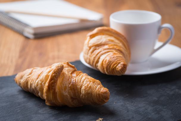 Dos sabrosos croissants franceses con una taza de café y un cuaderno
 - Foto, Imagen