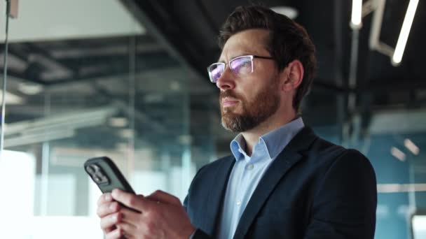 A modern okostelefont használó Earnest irodavezető üzenetet ír kortárs környezetben dolgozó kollégáinak. Demure munkáltató visel védő szemüveg gépelés kéznél digitális szerkentyű. - Felvétel, videó
