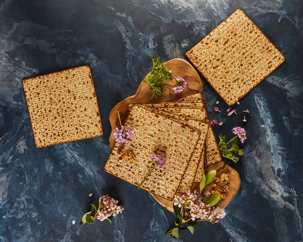 A Páscoa é a Páscoa judaica. Uma pilha de pão matzo exibida em uma placa de corte de madeira com um belo arranjo de flores e nozes, criando uma paisagem cênica de arte culinária - Foto, Imagem