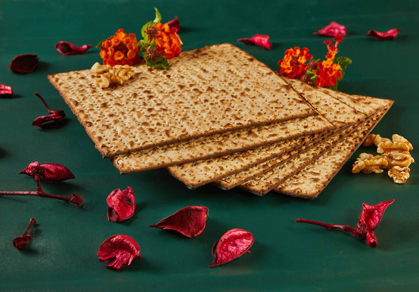 A Páscoa é a Páscoa judaica. Uma exibição de artes criativas com uma pilha de pão matzo com nozes e flores em uma mesa, cercado por têxteis folhosos e utensílios de mesa elegantes - Foto, Imagem