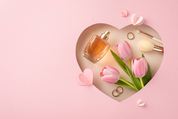 Conjunto Chic Mother 's Day: Vista superior de tulipas, perfume, ferramentas de maquiagem, acessórios de ouro e corações de papel em uma moldura em forma de coração contra o pano de fundo rosa pastel, perfeito para saudações ou promoções - Foto, Imagem