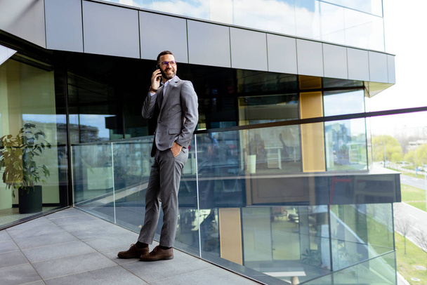 Homem adequado com braços cruzados está orgulhosamente diante de um edifício elegante, refletindo ambição. - Foto, Imagem