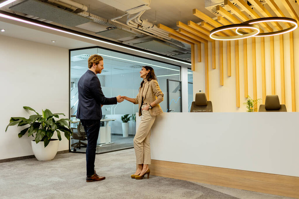 洗練されたオフィス環境でフレンドリーな握手で挨拶をする2人のプロフェッショナル - 写真・画像