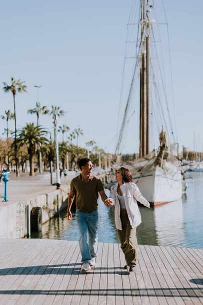 Cuple disfruta de un tranquilo paseo junto a barcos amarrados en el tranquilo puerto deportivo de Barcelona, disfrutando de la suave luz de la mañana. - Foto, imagen