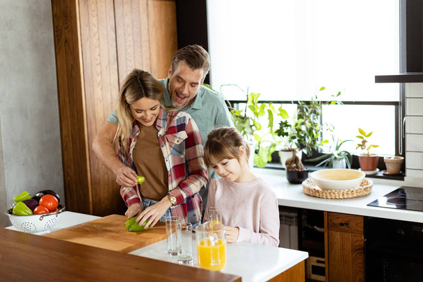 Young family chatting and preparing food around a bustling kitchen counter filled with fresh ingredients and cooking utensils - Photo, Image