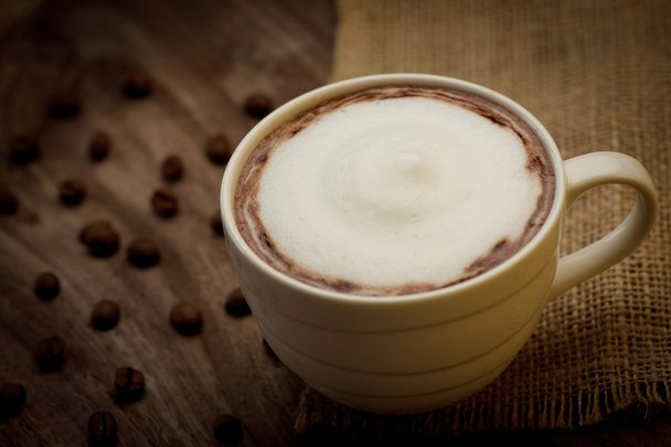 Чашка капучино подається на дерев'яному столі з кавовими зернами в
 - Фото, зображення