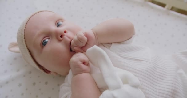 プランプ頬と大きな青い目を持つ愛らしい新生児は,体を動かしてカメラを見ています. ベッドシートに横たわる甘い美しい新生児,演劇はつま先笑顔を見るカメラに触れる. - 映像、動画