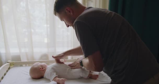 Jongeman vader zachtjes masseren buik van schattige baby 's op een commode in de kinderkamer. Papa brengt tijd door met pasgeboren baby 's en zorgt voor hem. Ouderschap als concept - Video