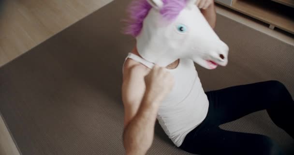 Uomo divertente con maschera di unicorno che fa esercizio per il rilassamento miofasciale a casa. fitness comico a casa. Concetto di salute e fitness. Dolore alla schiena durante una pausa pranzo. - Filmati, video