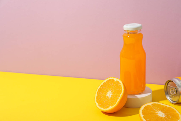 Glazen fles met sap en sinaasappels op roze achtergrond, ruimte voor tekst - Foto, afbeelding