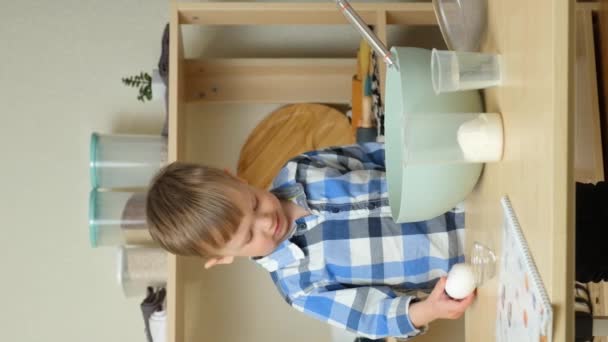 Dwuletni chłopiec rozbija surowe jajko na ciasto. Małe dzieci w kuchni, pionowe zwolnione ruchy - Materiał filmowy, wideo