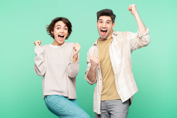 Young couple two friends family man woman wear casual clothes looking camera together do winner gesture celebrate clenching fists say yes isolated on turquoise colour background studio - Photo, Image