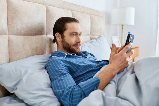 Ένας άντρας διαλογίζεται ήσυχα στο κρεβάτι με ένα κινητό στο χέρι.. - Φωτογραφία, εικόνα