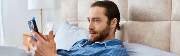 Een man ontspannen in bed, mindfulness oefenen met zijn mobiele telefoon in de hand. - Foto, afbeelding