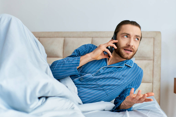 Мужчина лежит в постели, разговаривает по мобильному телефону утром. - Фото, изображение