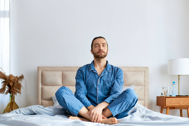 Schöner Mann praktiziert morgens Yoga mit überkreuzten Beinen auf dem Bett. - Foto, Bild