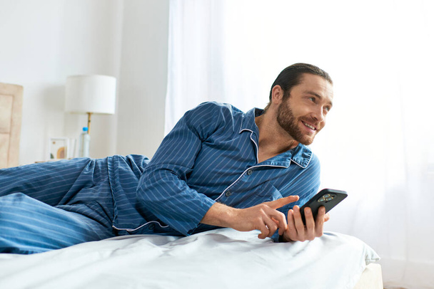 Człowiek pokojowo zaangażowany z telefonem komórkowym leżąc na wygodnym łóżku. - Zdjęcie, obraz