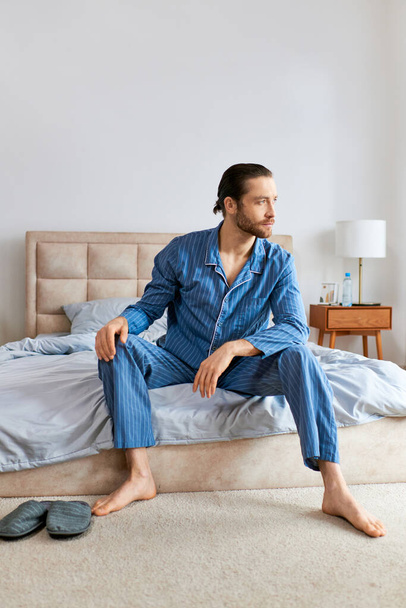 Przystojny mężczyzna w piżamie siedzi spokojnie na łóżku. - Zdjęcie, obraz