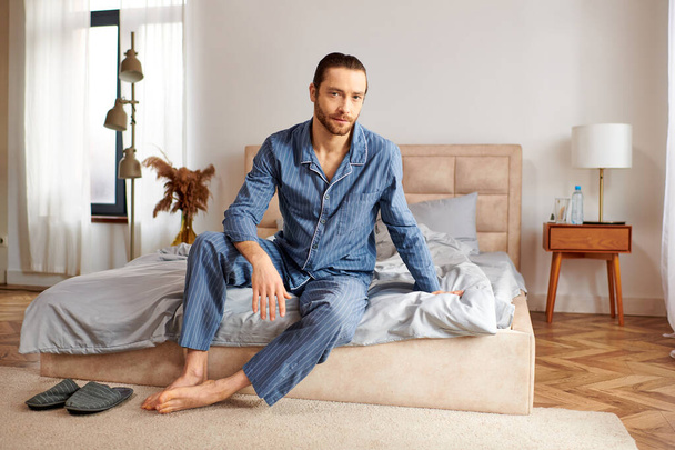 Jóképű férfi ül az ágyon a kényelmes hálószobában. - Fotó, kép